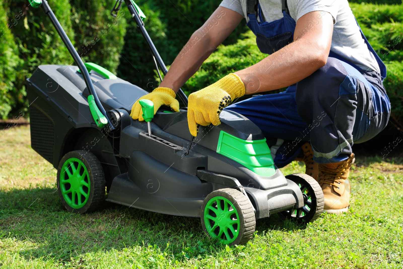 Photo of Young man with screwdriver fixing lawn mower in garden, closeup