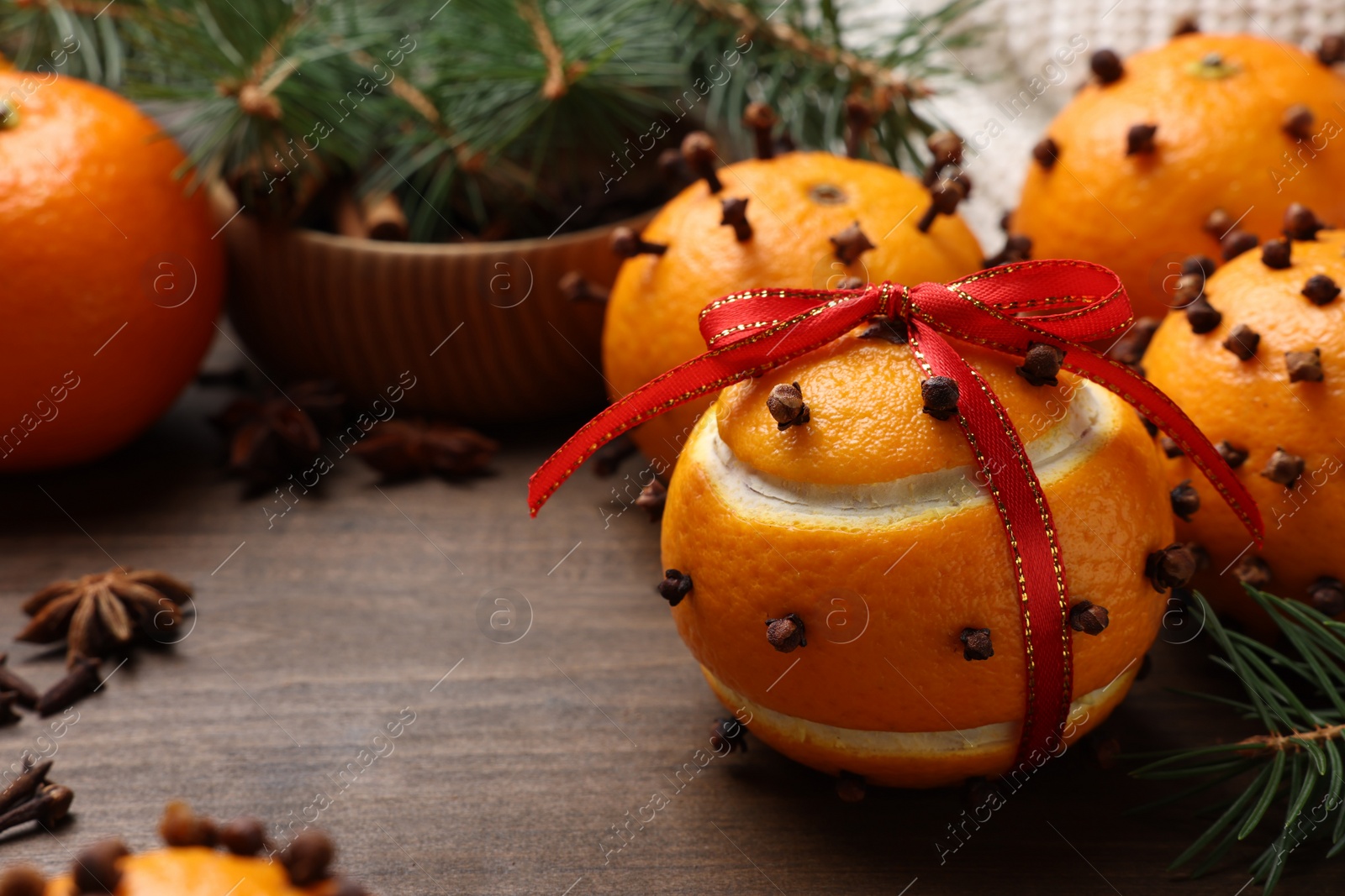 Photo of Pomander balls made of tangerines with cloves and fir branches on wooden table, closeup. Space for text