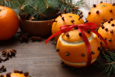 Pomander balls made of tangerines with cloves and fir branches on wooden table, closeup. Space for text