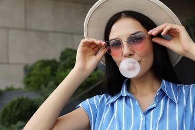 Stylish woman blowing gum near building outdoors