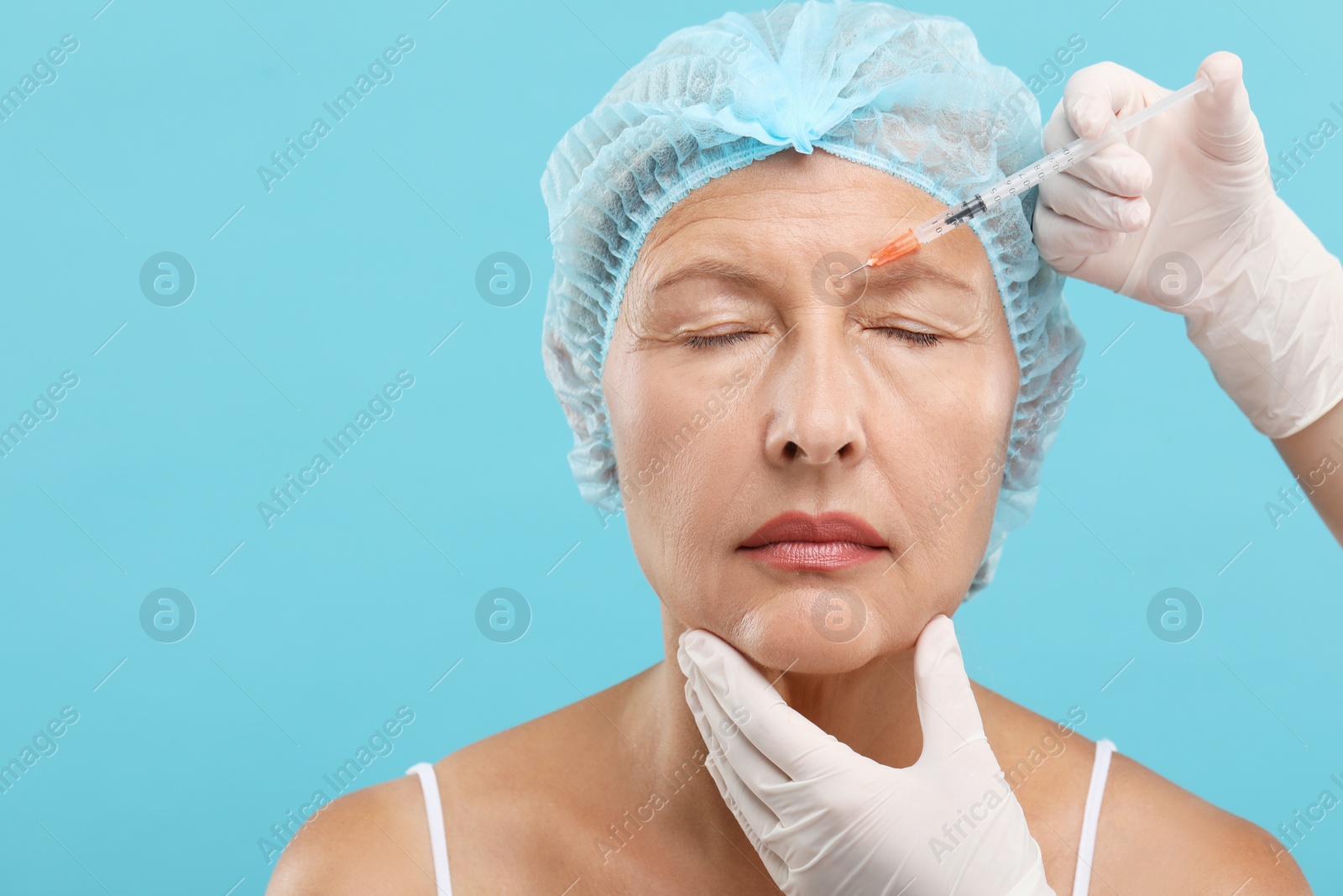 Photo of Doctor giving facial injection to senior woman on light blue background. Cosmetic surgery