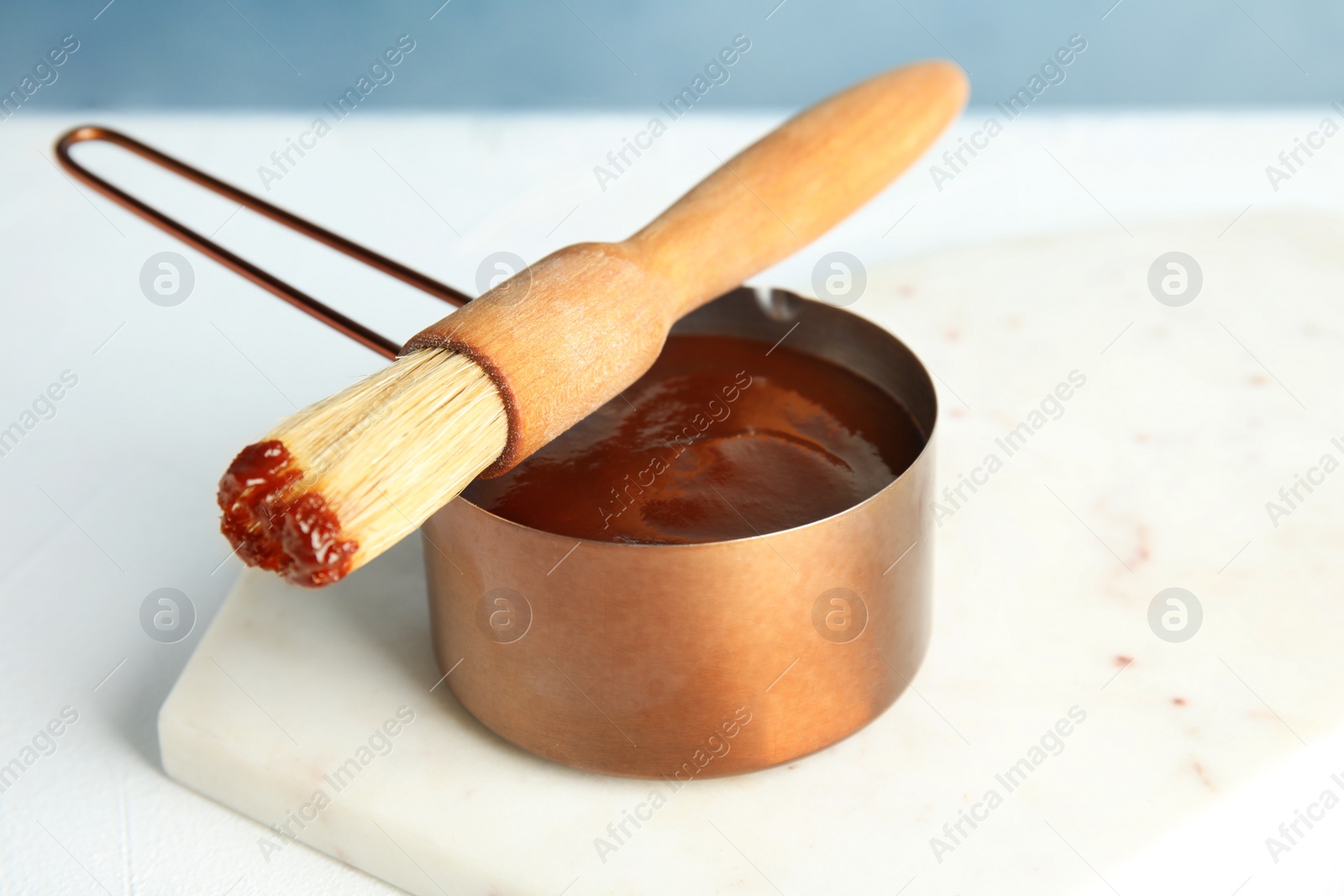 Photo of Cooking pot with barbecue sauce and brush on white table