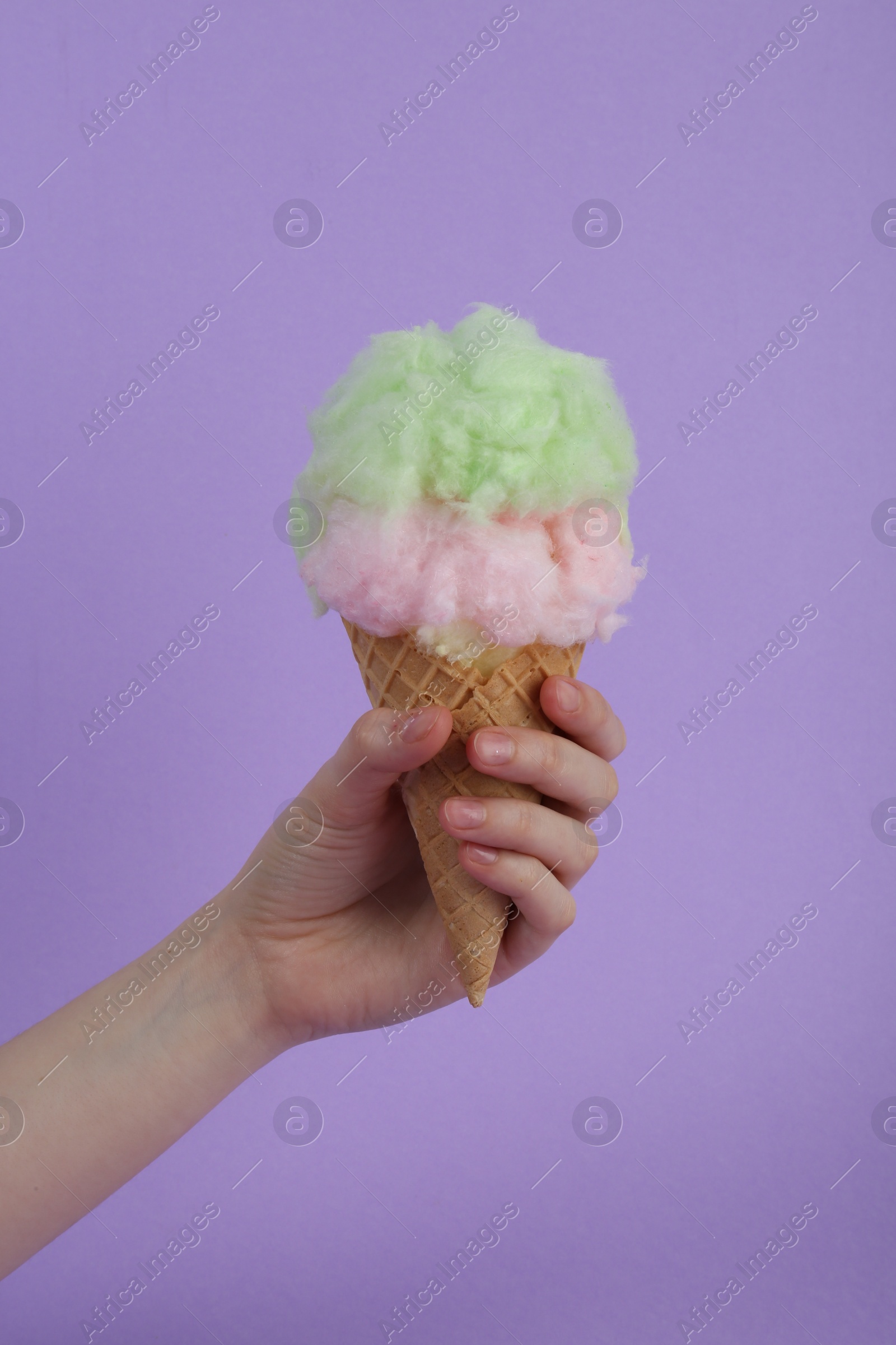 Photo of Woman holding waffle cone with cotton candy on violet background, closeup