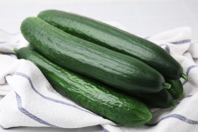 Photo of Fresh cucumbers and cloth on white table, closeup