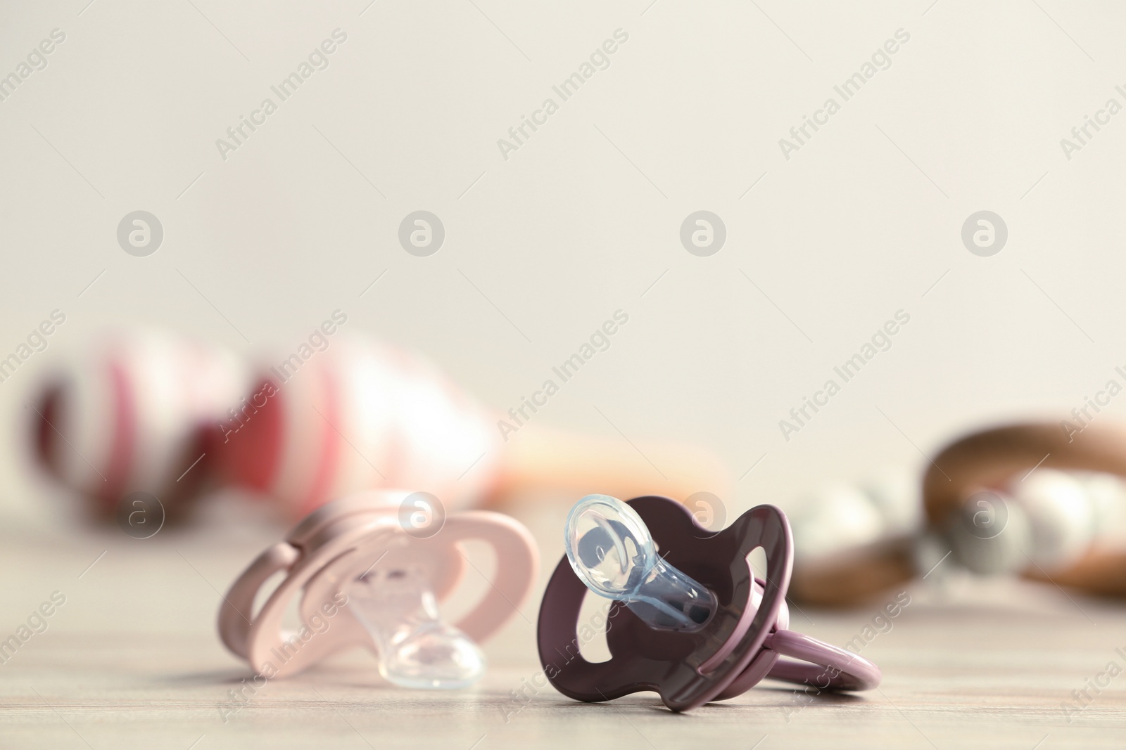 Photo of Baby pacifiers on beige table against blurred background, space for text