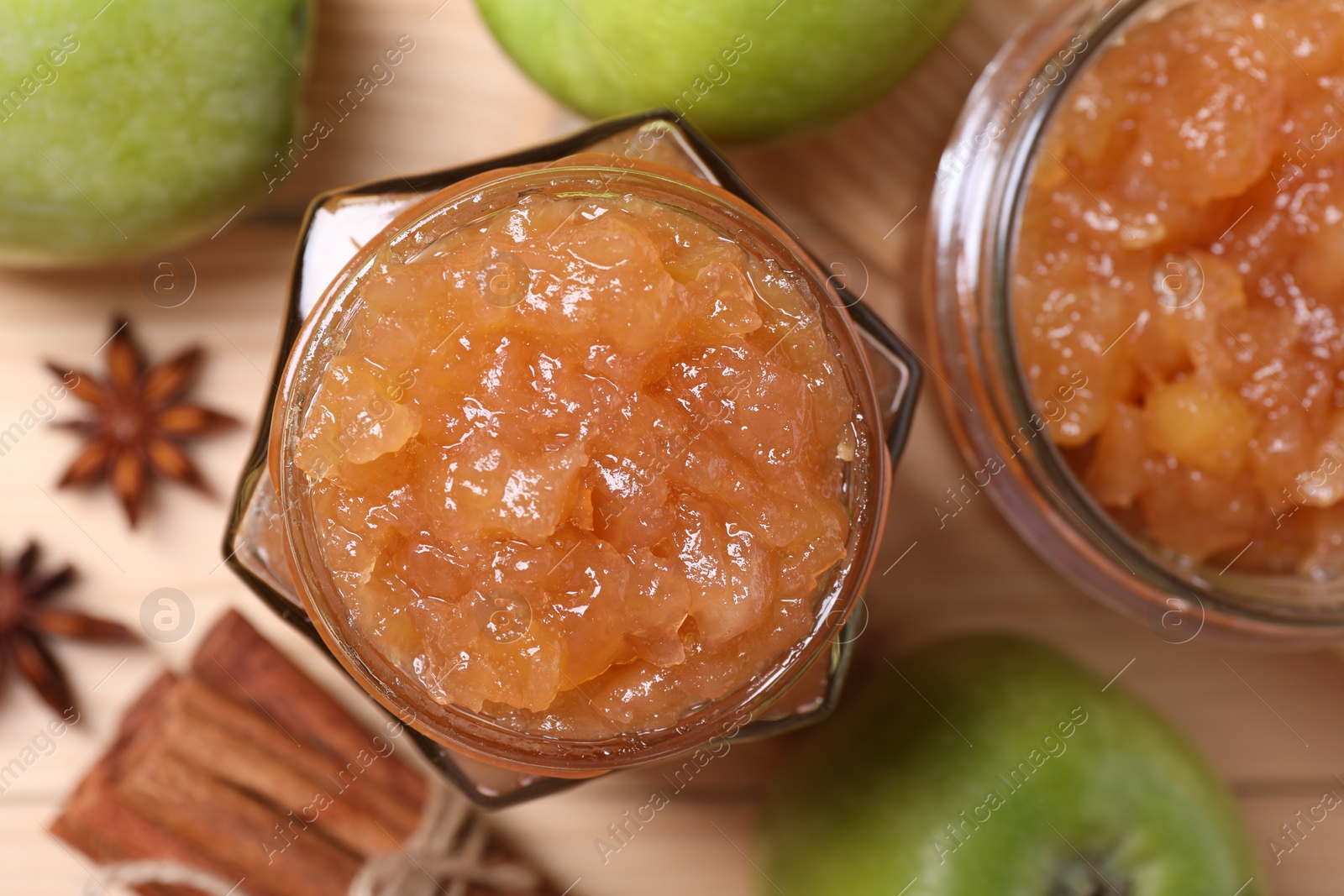 Photo of Delicious apple jam in jars, fresh fruits and spices on wooden table, flat lay