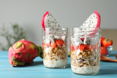 Granola with strawberries and pitahaya in glass jars on  light blue wooden table