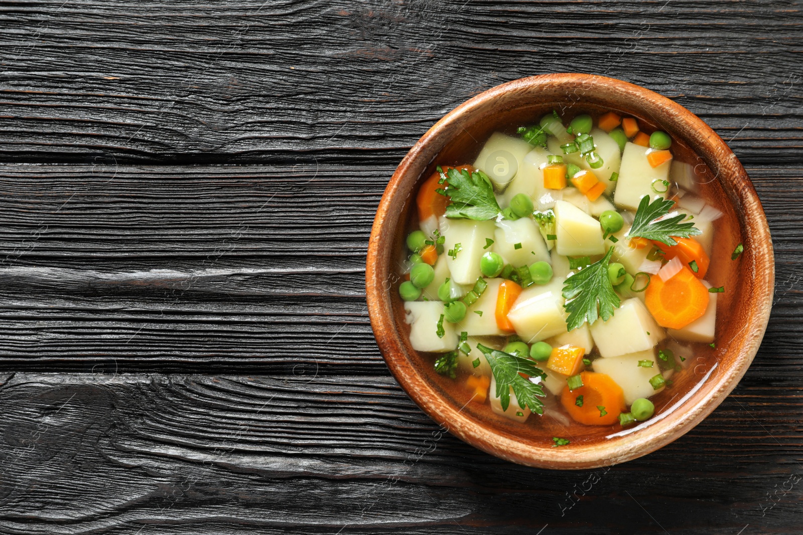 Photo of Bowl of fresh homemade vegetable soup on dark wooden background, top view. Space for text