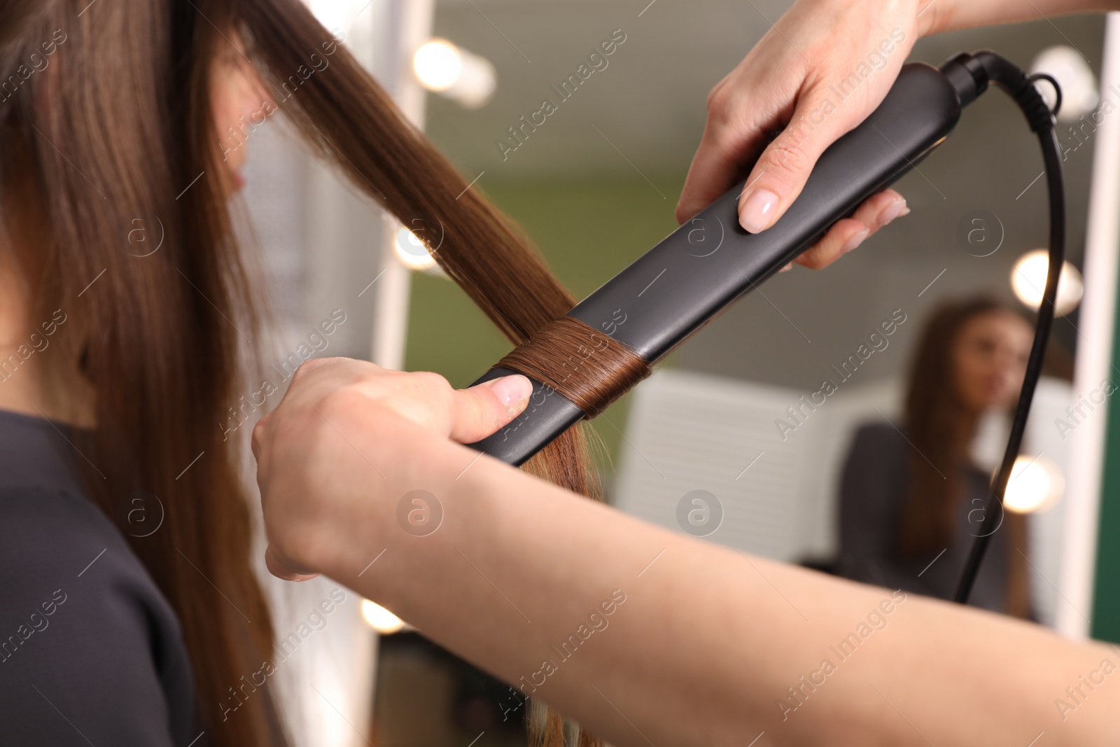 Photo of Stylist curling woman's hair with flat iron in salon