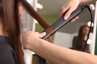 Photo of Stylist curling woman's hair with flat iron in salon