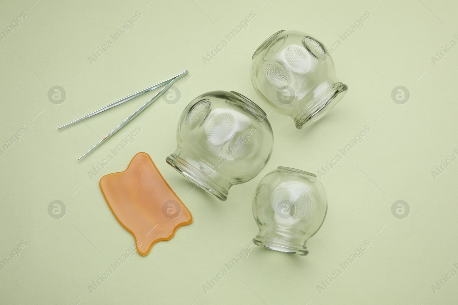 Photo of Glass cups, gua sha and tweezers on light olive background, flat lay. Cupping therapy