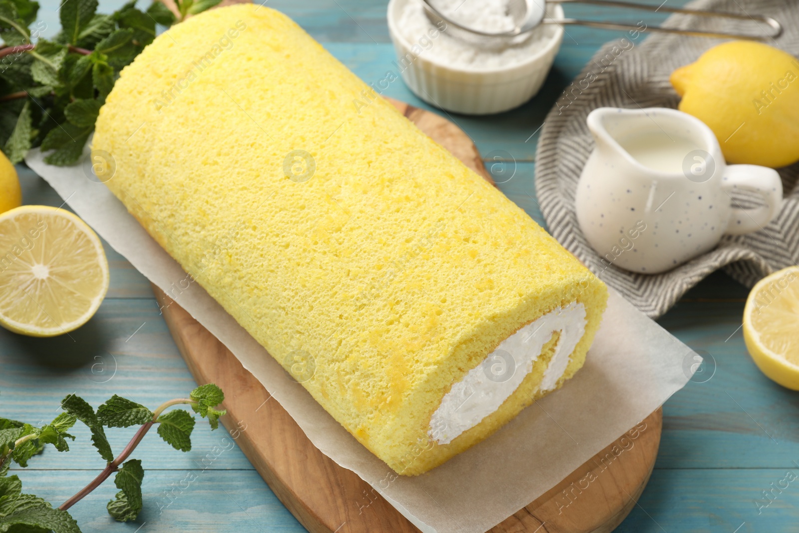 Photo of Delicious cake roll, mint, lemons and powdered sugar on light blue wooden table, closeup