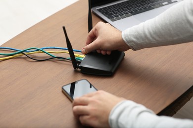 Photo of Man with smartphone connecting to internet via Wi-Fi router at wooden table, closeup