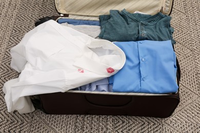 Men's shirt with lipstick kiss marks among other clothes in suitcase on carpet