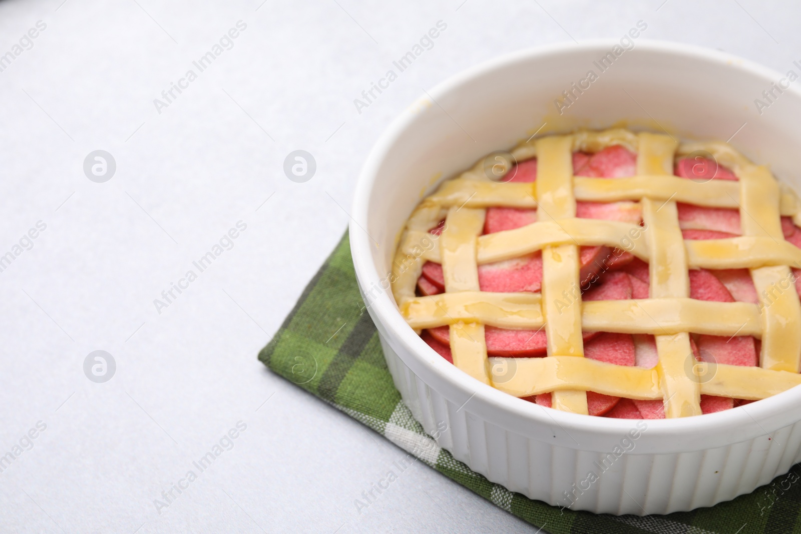 Photo of Baking dish with raw apple pie on light table, closeup. Space for text