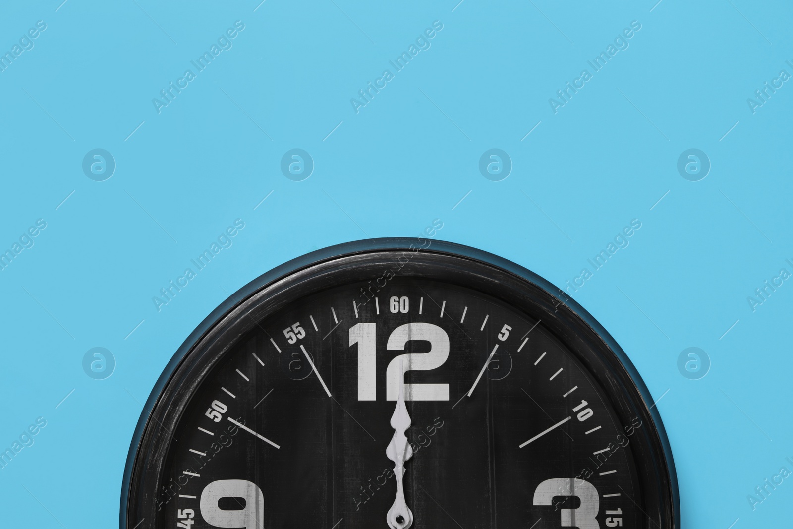 Photo of Stylish analog clock hanging on light blue wall, space for text