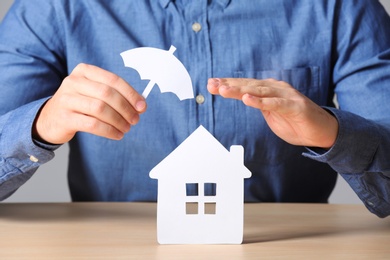 Male insurance agent covering paper home with umbrella cutout at table, closeup