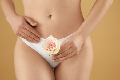 Photo of Gynecology. Woman in underwear with rose flower on beige background, closeup