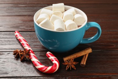 Tasty hot chocolate with marshmallows, candy cane and spices on wooden table, closeup