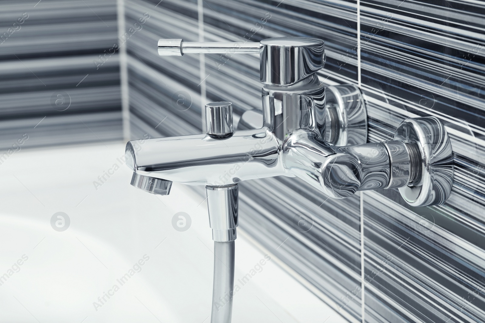 Photo of Shiny bath water tap installed on black and white wall