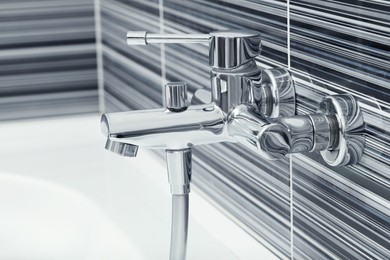 Photo of Shiny bath water tap installed on black and white wall