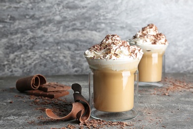 Glass cups of tasty coffee with whipped cream on gray table