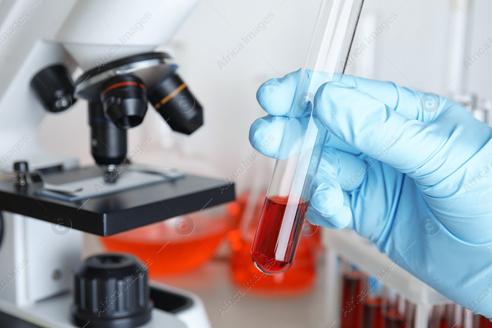 Image of Scientist holding test tube with blood sample near microscope, closeup. Laboratory analysis