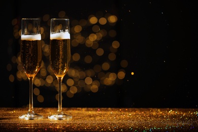 Glasses of champagne and golden glitter on table against blurred background. Space for text