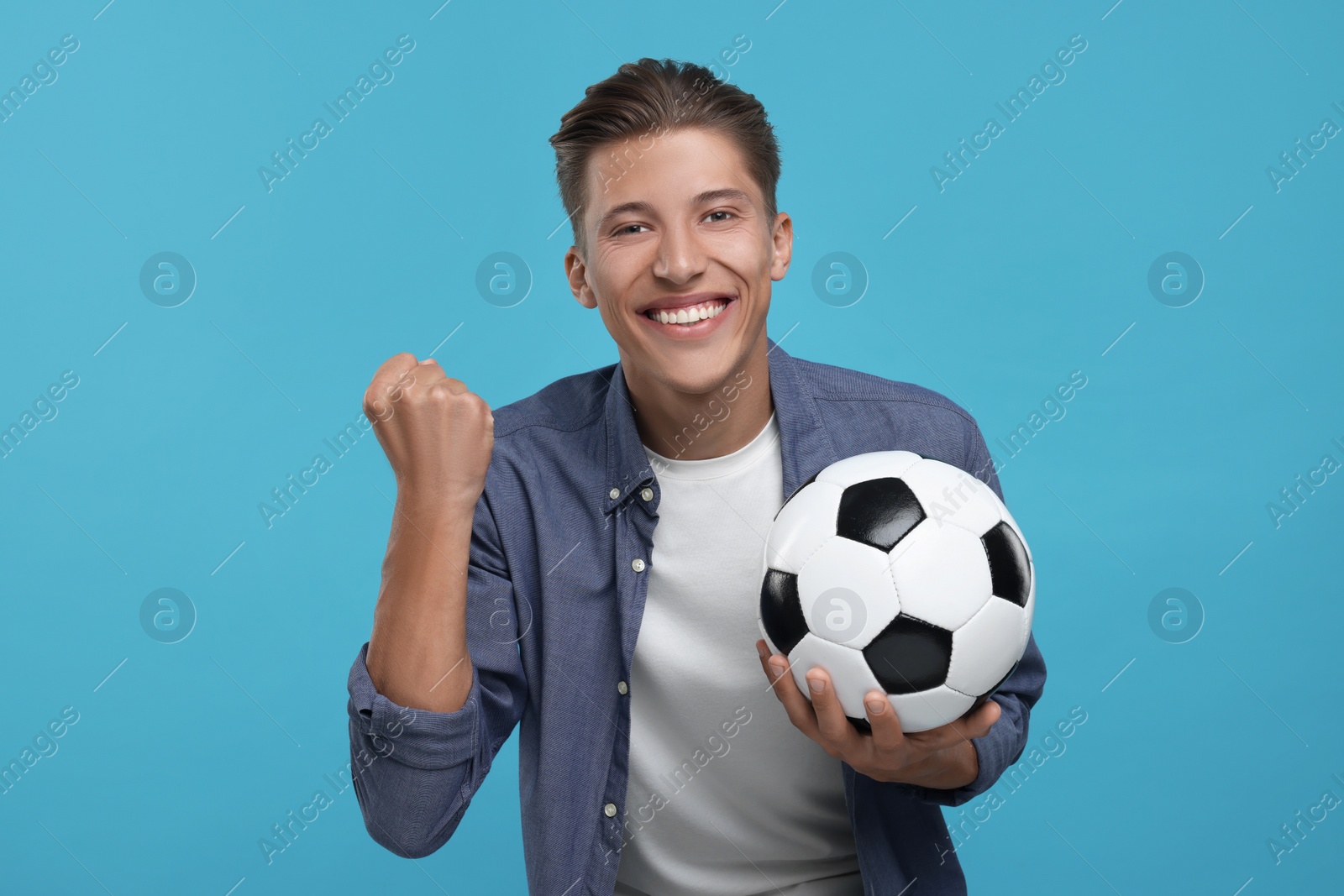 Photo of Happy sports fan with soccer ball celebrating on light blue background