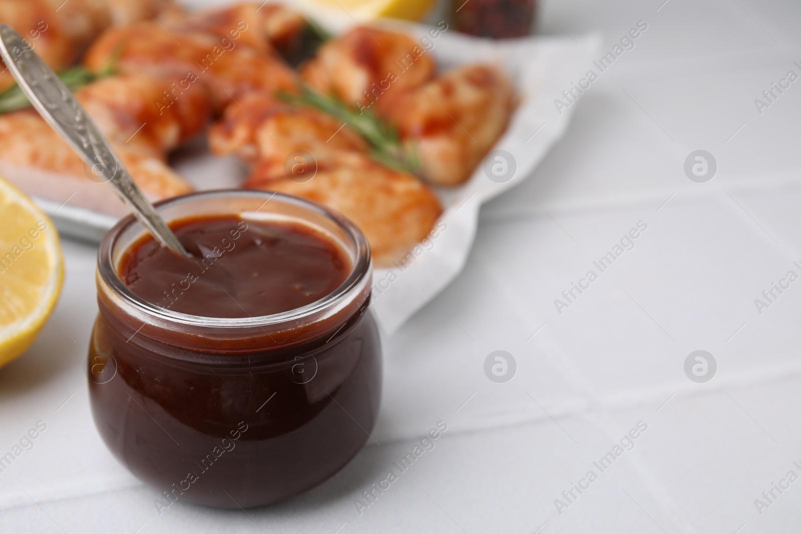 Photo of Fresh marinade with spoon in jar on light tiled table, closeup. Space for text