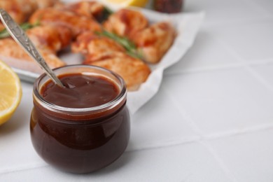 Photo of Fresh marinade with spoon in jar on light tiled table, closeup. Space for text