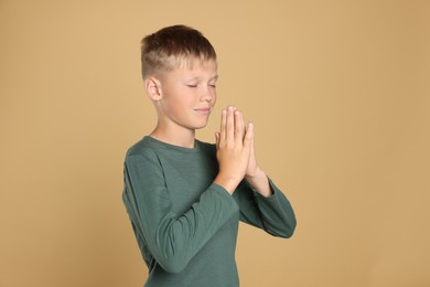Photo of Boy with clasped hands praying on beige background