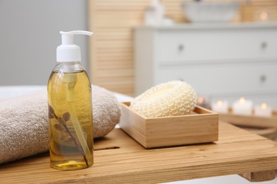 Photo of Dispenser of liquid soap, towel and loofah on bath tray indoors. Space for text