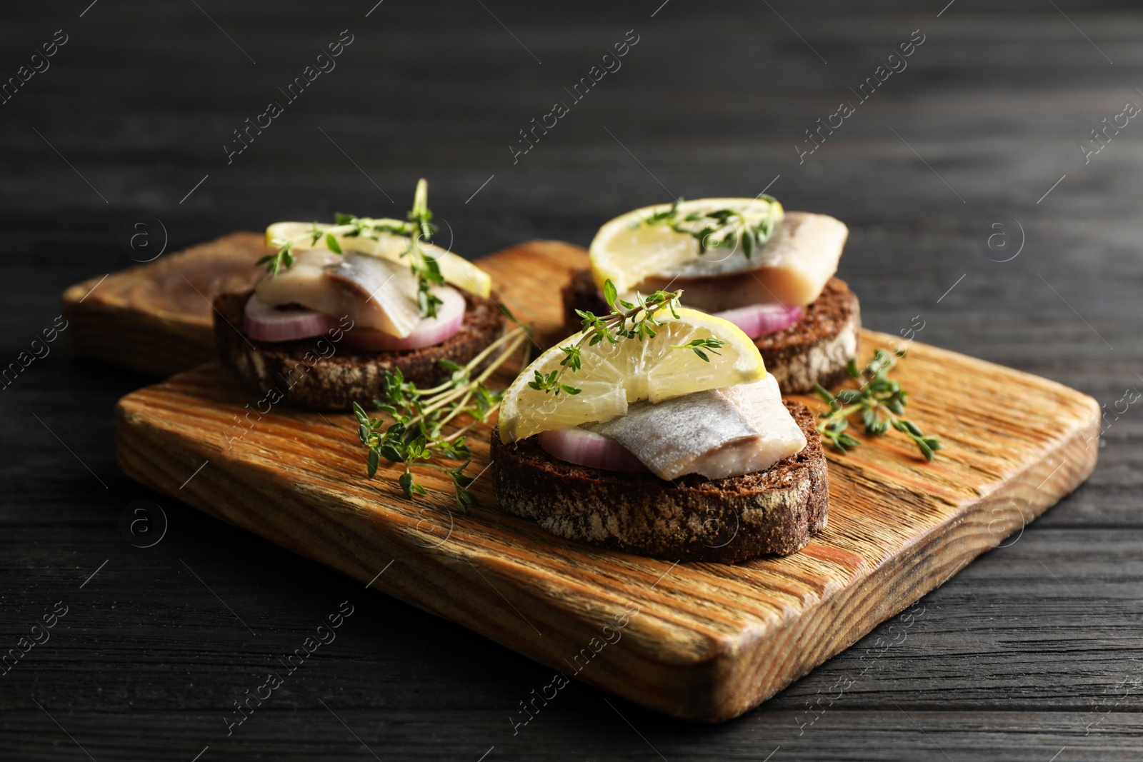 Photo of Delicious sandwiches with salted herring, onion rings, thyme and lemon on dark wooden table, closeup