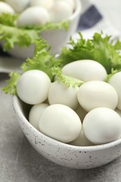 Photo of Peeled boiled quail eggs in bowl on grey table, closeup