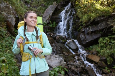 Photo of Tourist with backpack and bottle near waterfall in mountains. Space for text