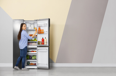 Young woman taking juice out of refrigerator indoors, space for text