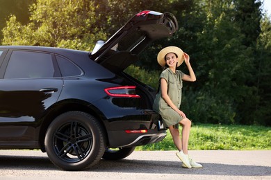 Happy woman sitting in trunk of modern car outdoors