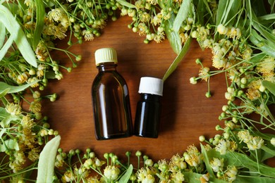 Photo of Bottles of essential oil and linden blossoms on wooden table, flat lay