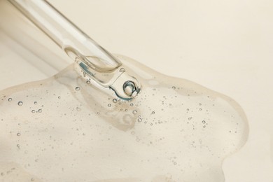 Dripping cosmetic oil from pipette onto beige background, closeup