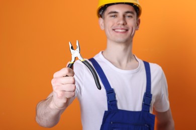 Photo of Young man holding pliers on orange background, selective focus