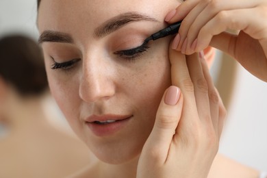 Photo of Makeup product. Woman applying black eyeliner on blurred background, closeup