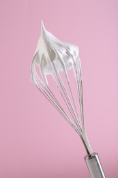 Whisk with whipped cream on pink background