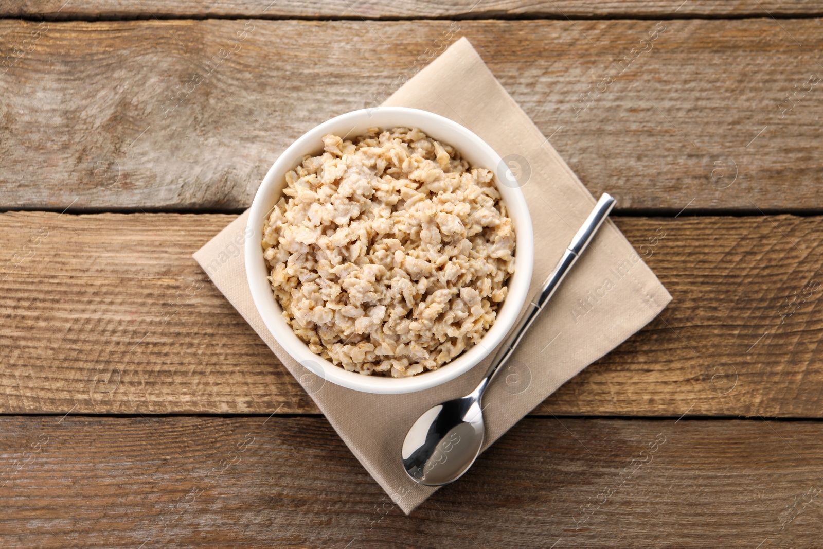 Photo of Tasty boiled oatmeal in bowl and spoon on wooden table, top view