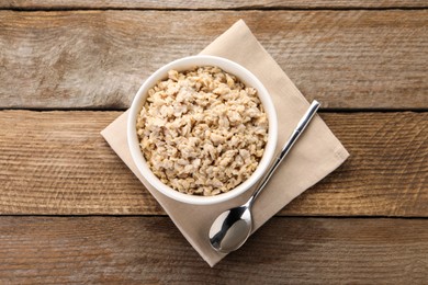 Photo of Tasty boiled oatmeal in bowl and spoon on wooden table, top view