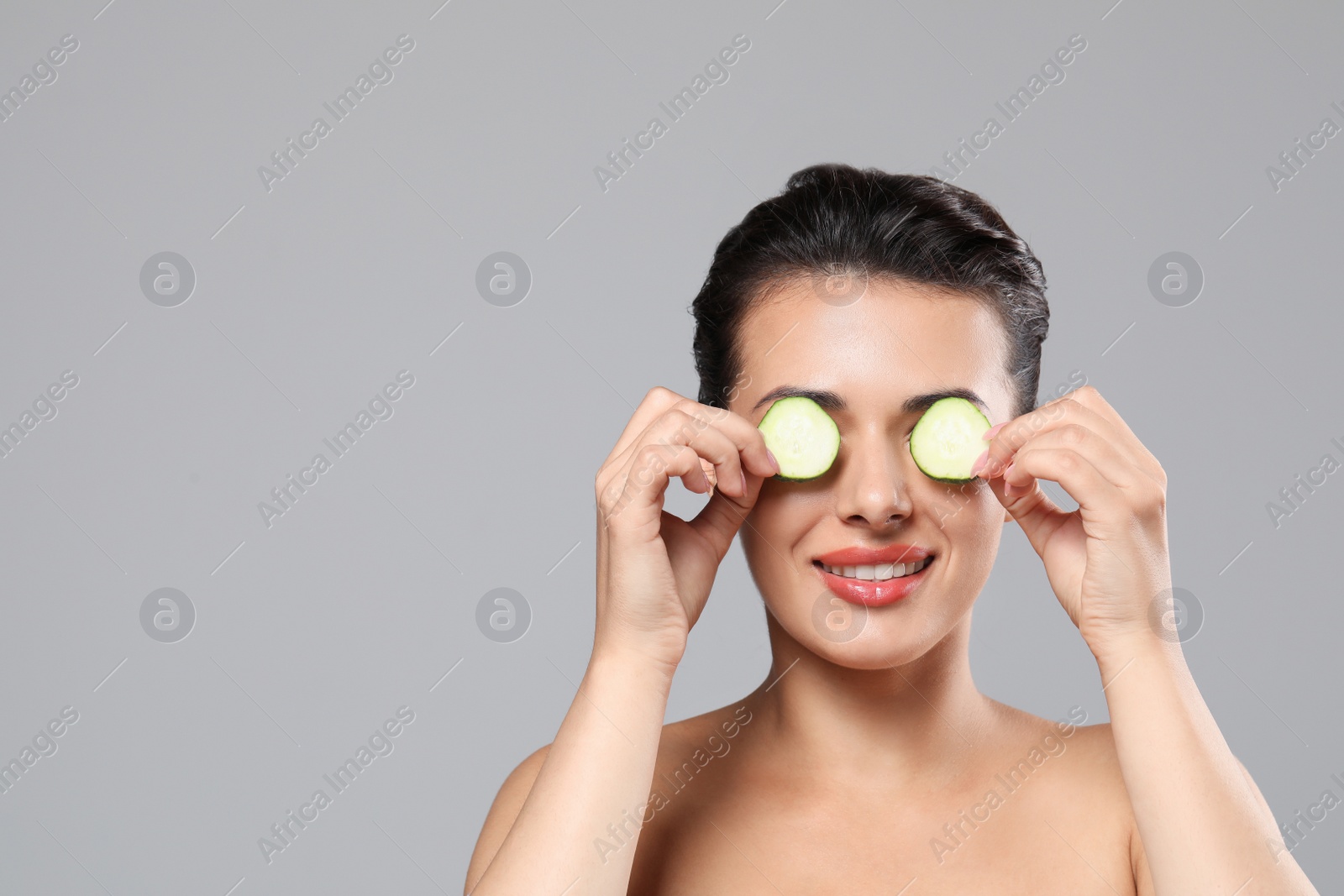 Photo of Woman covering eyes with cucumber slices on grey background, space for text. Skin care