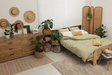 Stylish bedroom with comfortable bed and beautiful green houseplants, above view. Interior design