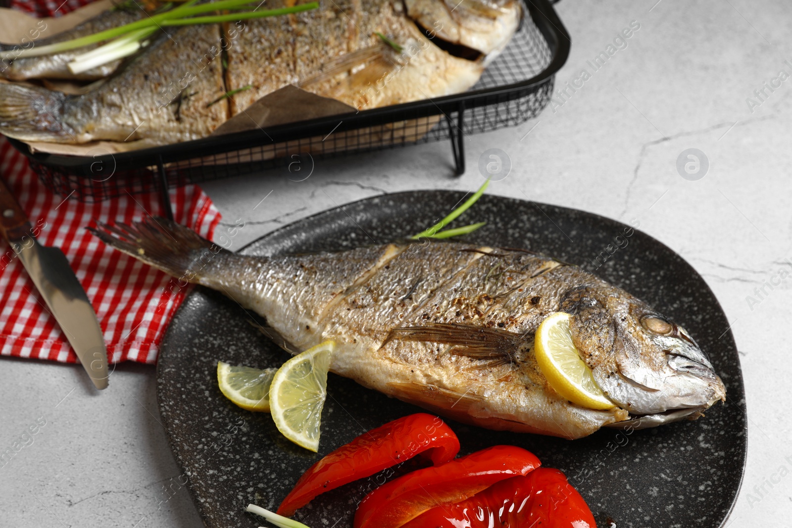 Photo of Delicious baked fish served with bell pepper and lemon on light textured table. Seafood