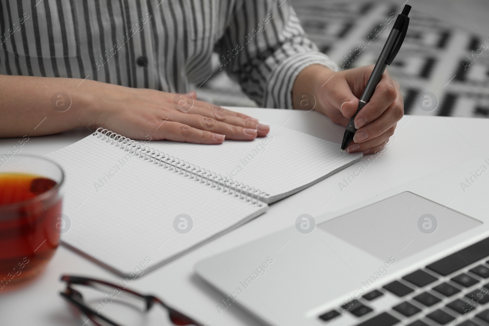 Photo of Left-handed woman writing in notebook at table indoors, closeup