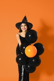 Beautiful woman wearing witch costume with balloons for Halloween party on yellow background